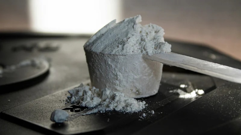 A plastic scoop heaped with white powder resting on a black weight plate