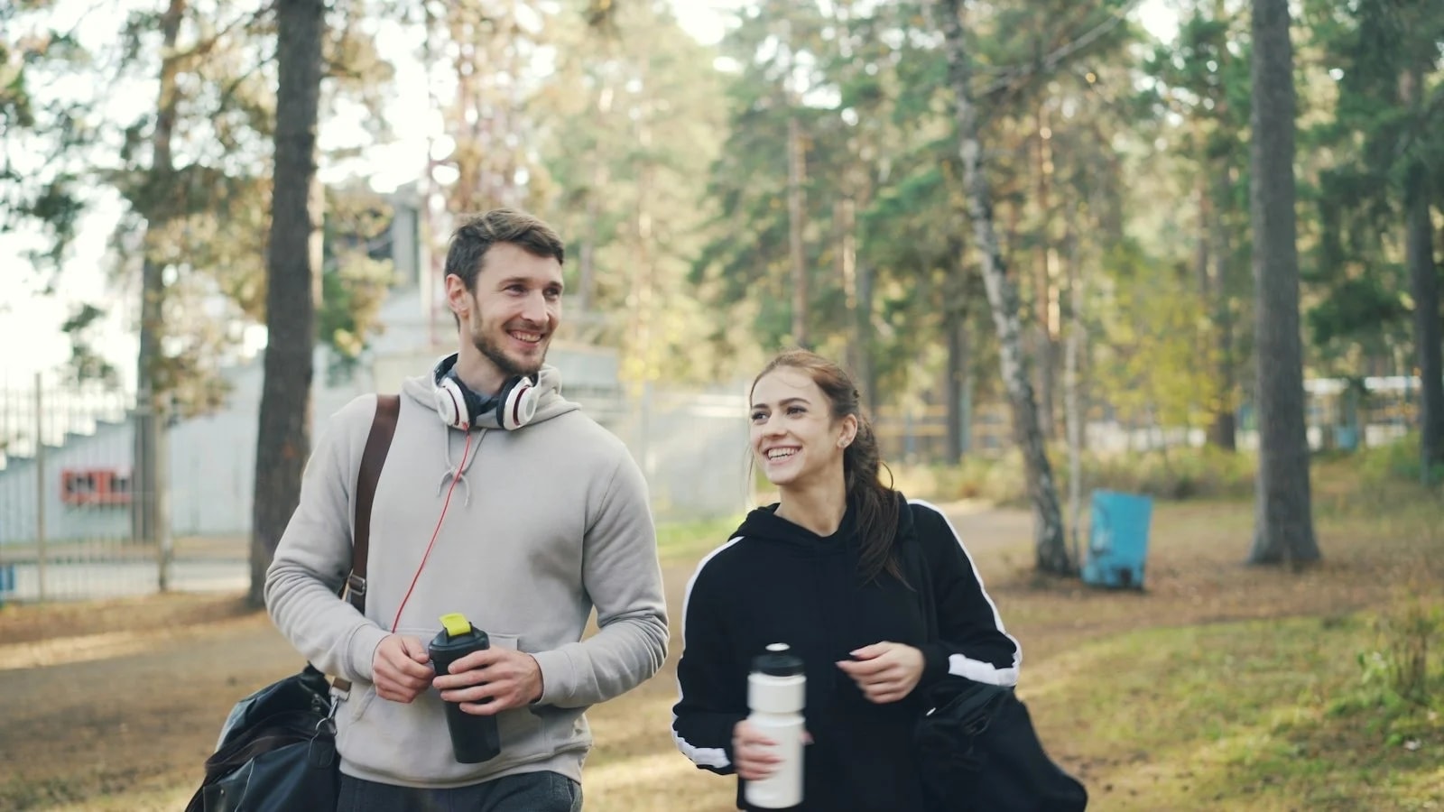A man and a woman walking through a park with gym bags and water bottles