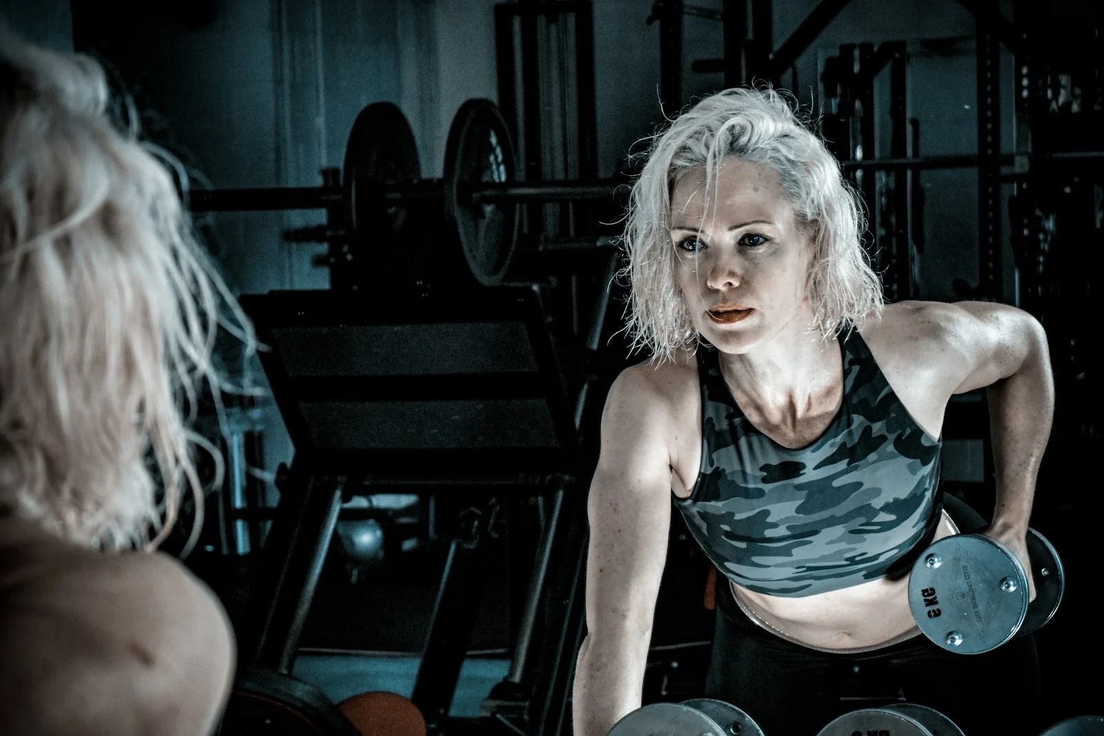 A woman with short blonde hair doing a one-arm dumbbell row in a gym