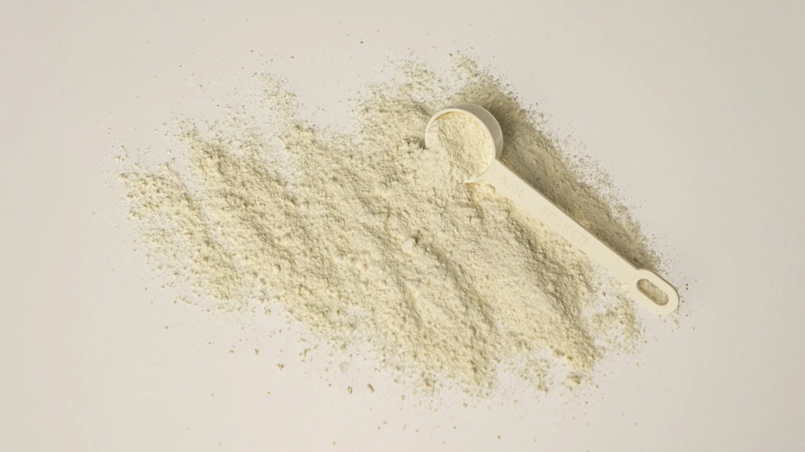 A small white scoop resting in a wide spread of pale powder on a white surface