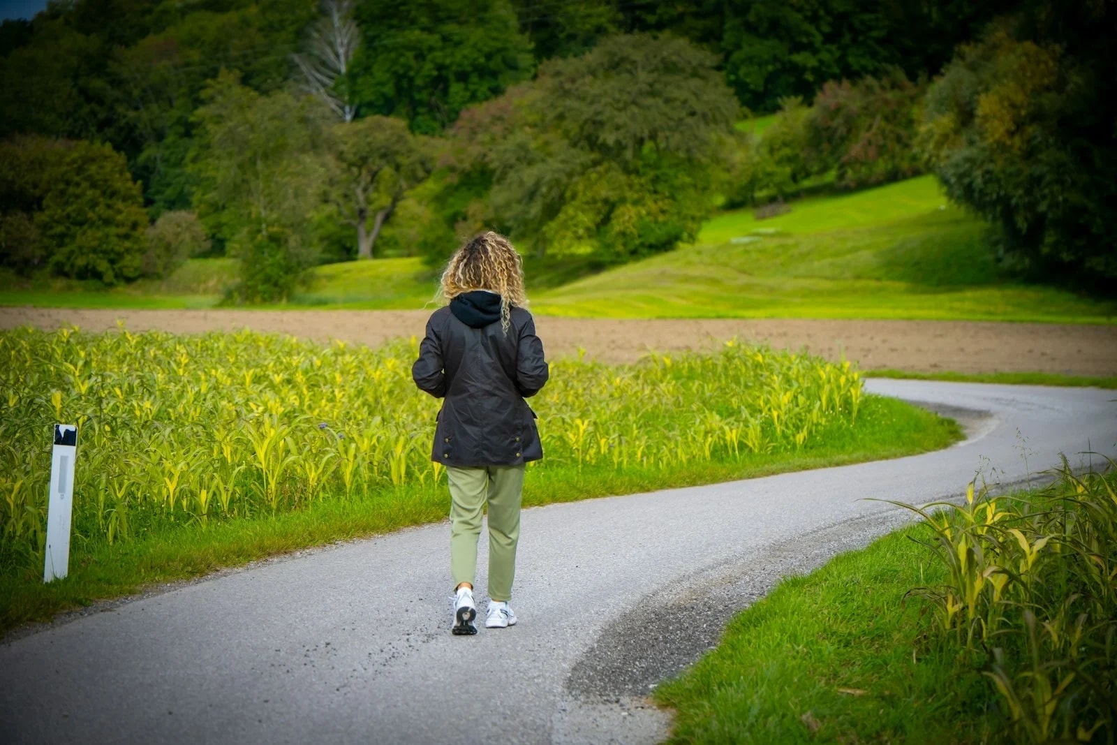 A woman in a dark jacket walking along a curving path through green fields