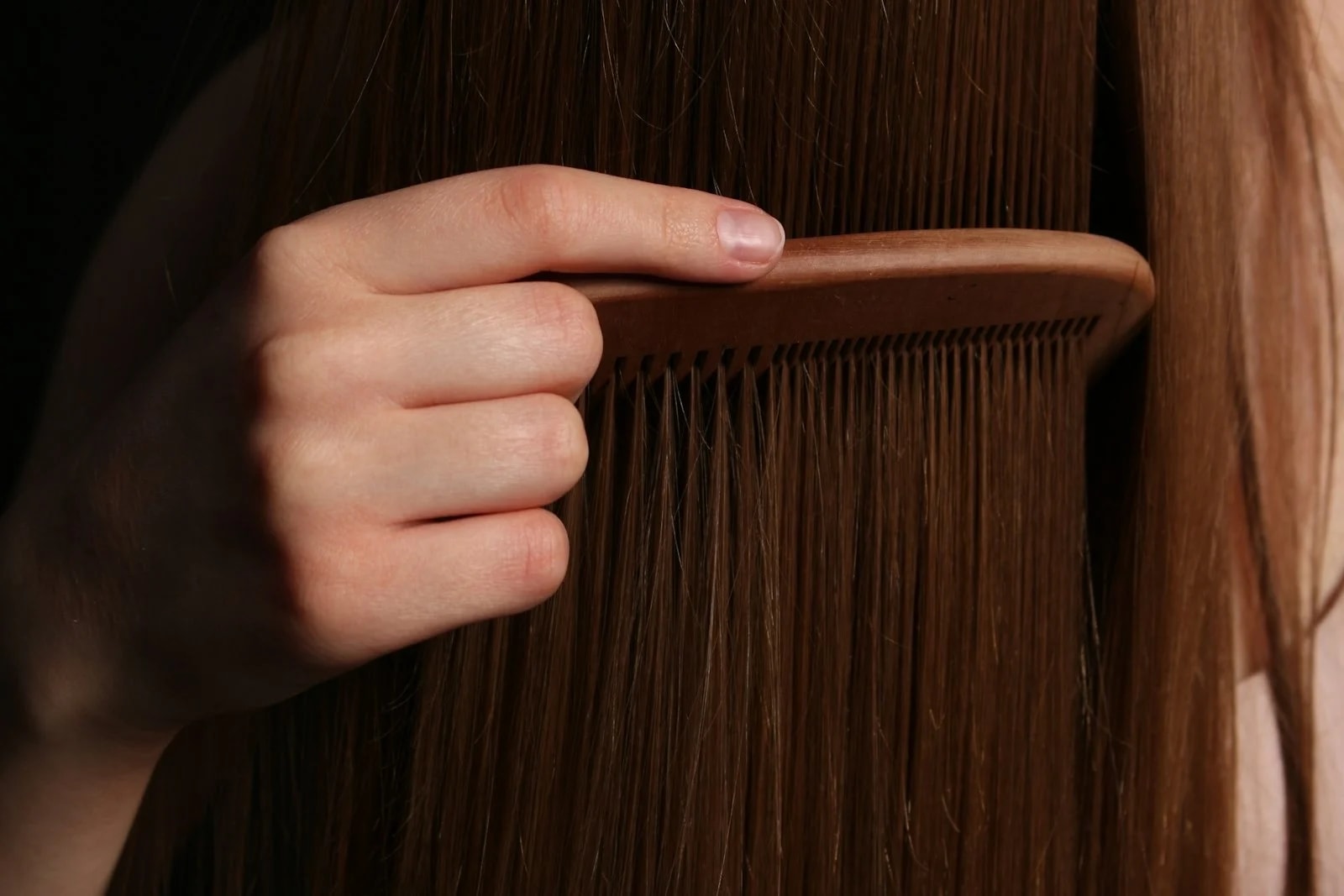 A hand running a wooden comb through long brown hair