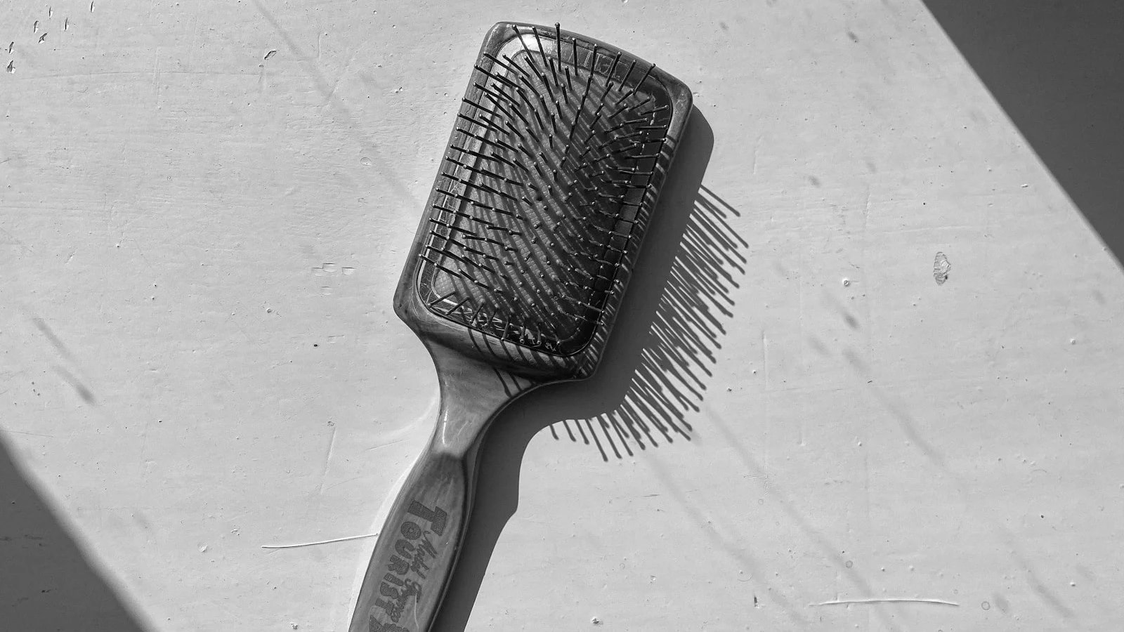 A black and white photo of a paddle hairbrush lying on a light surface