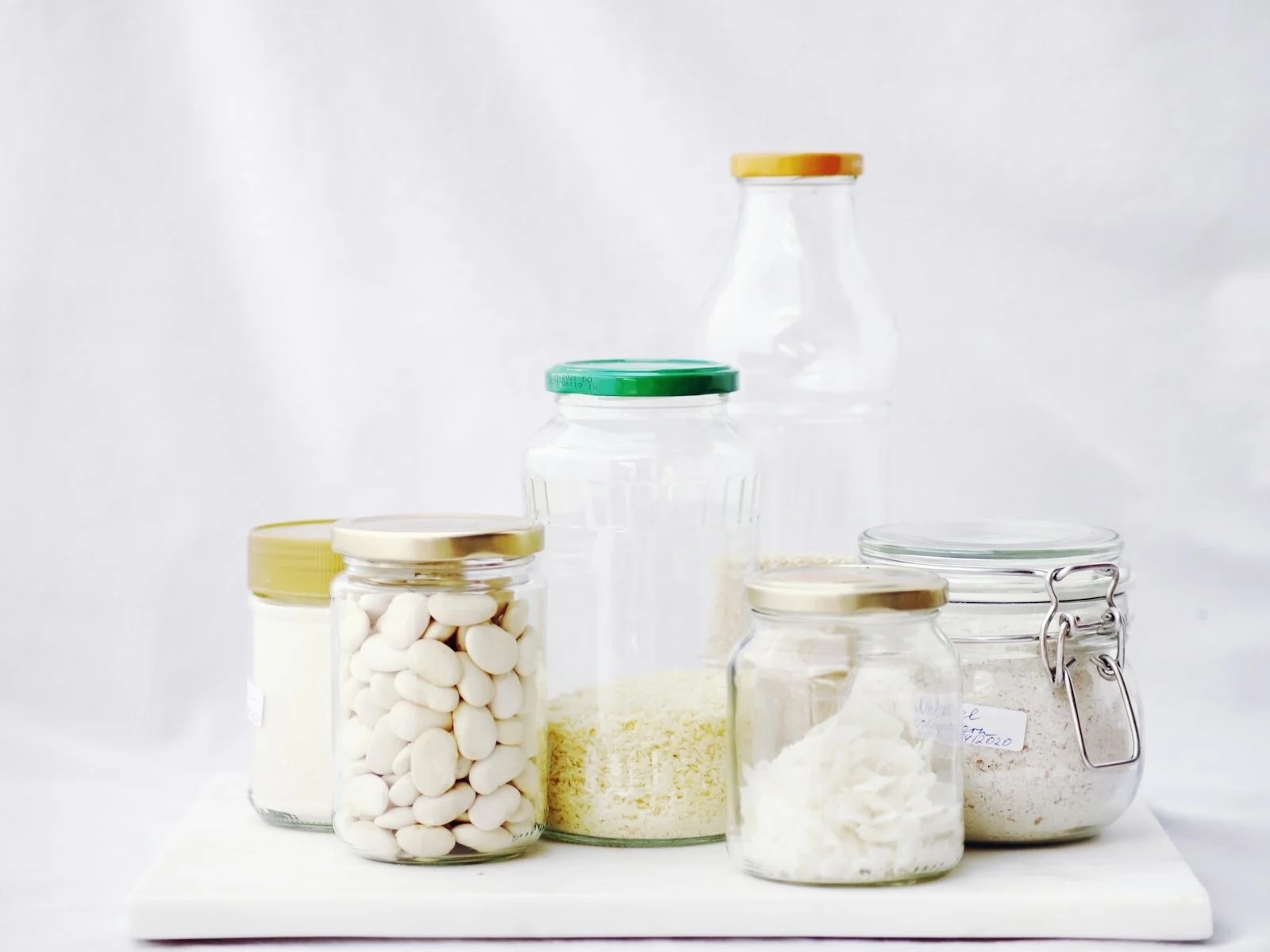 Glass jars with sealed lids holding dry foods on a white table