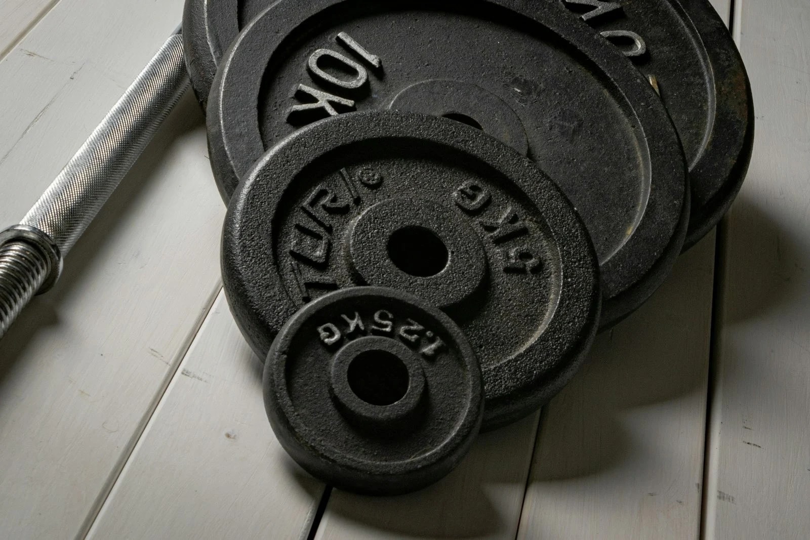 Iron weight plates of 10 kg, 5 kg and 1.25 kg stacked next to a barbell on a wooden floor