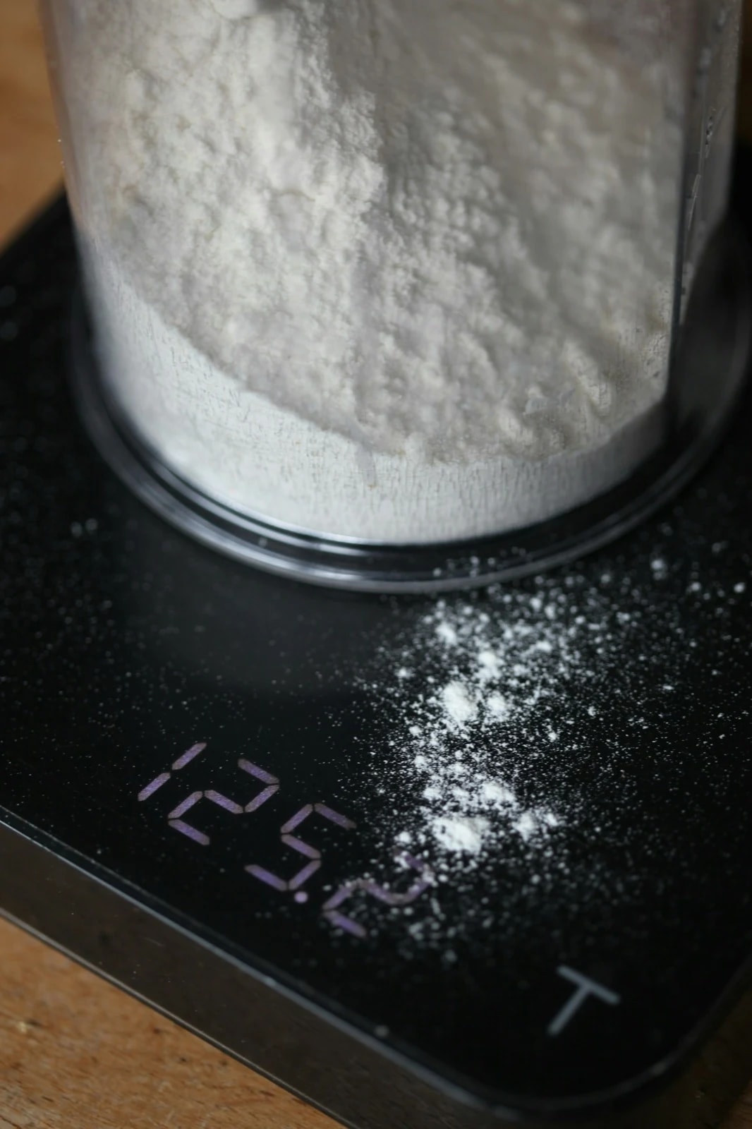 A container of white powder on a digital kitchen scale with a gram reading