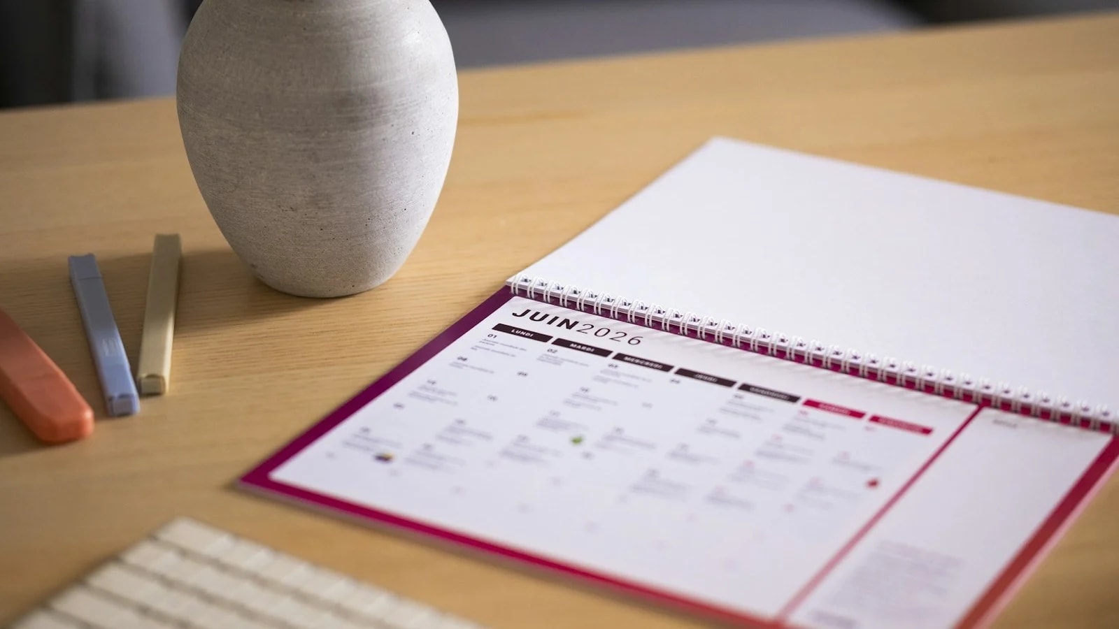 A monthly desk calendar open on a wooden table next to a ceramic vase