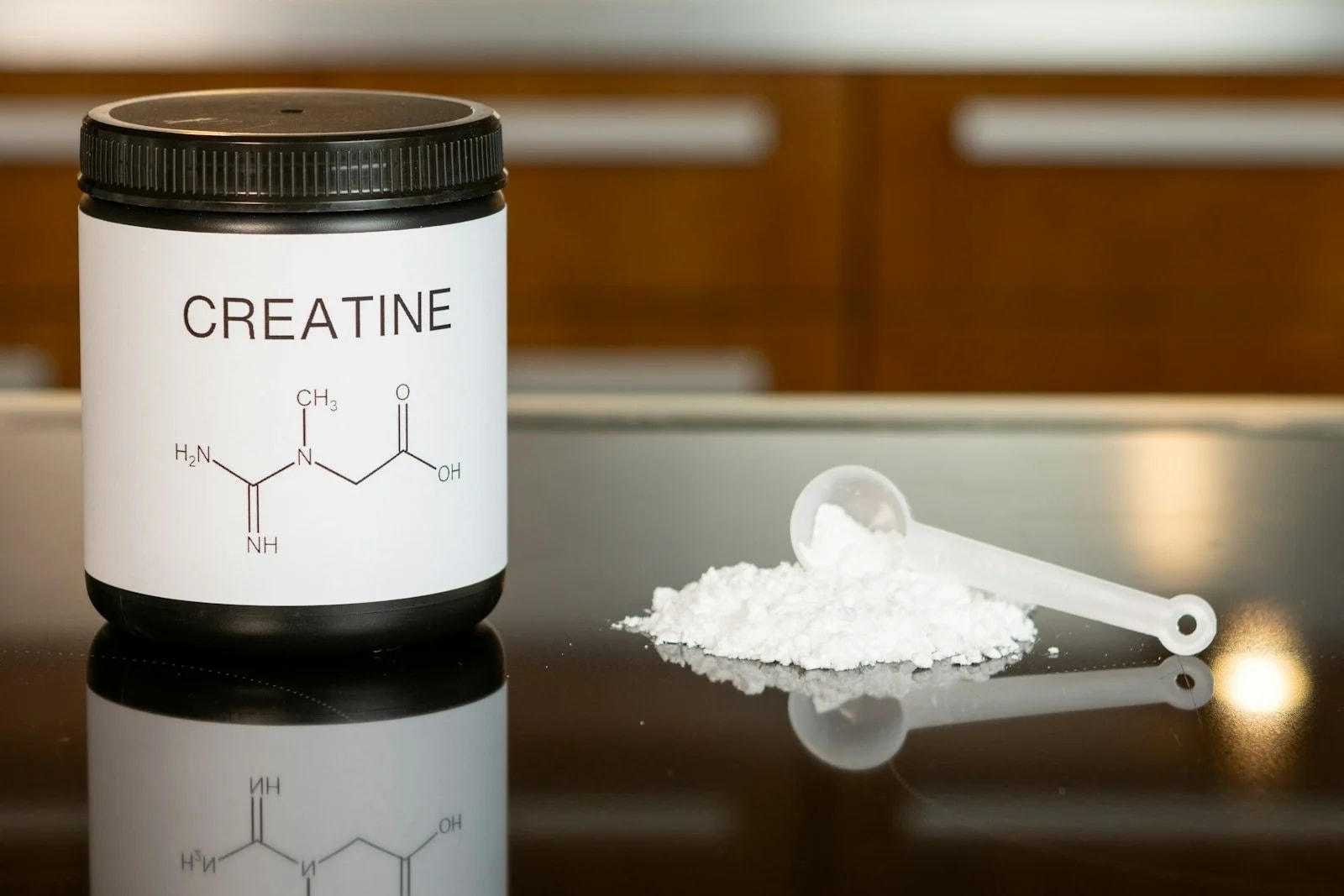 A plain jar labelled creatine next to a measuring scoop and a small pile of white powder