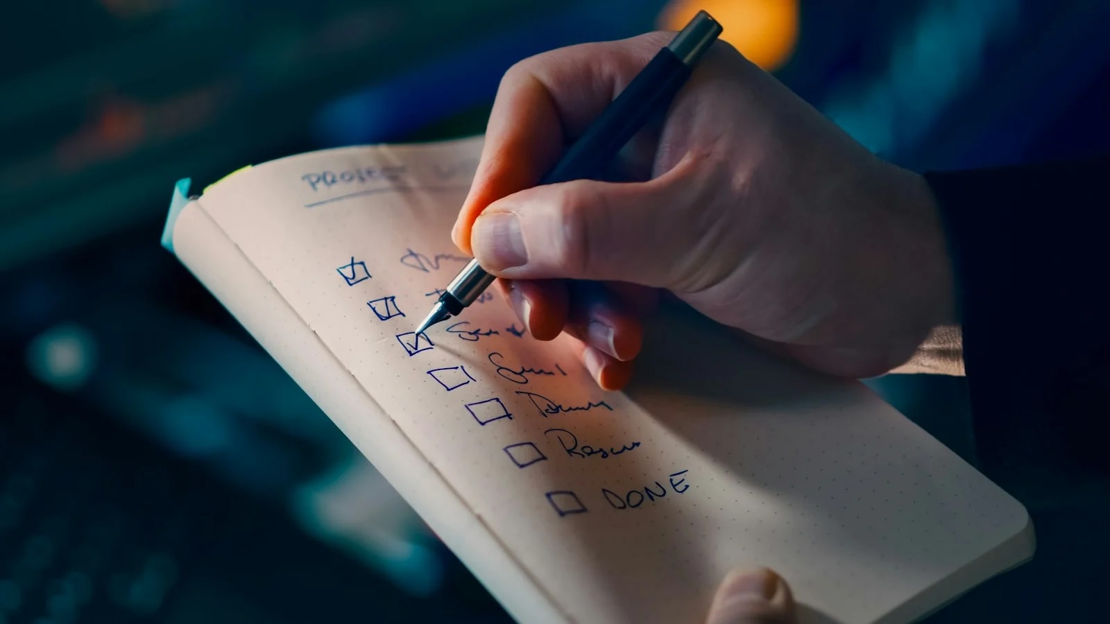 A hand ticking boxes on a handwritten checklist in a notebook