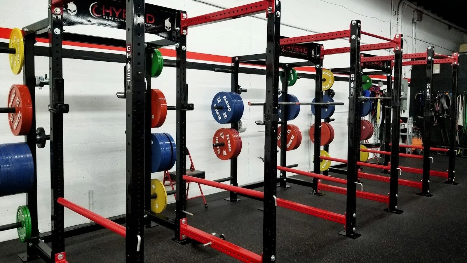 A row of red and black squat racks with colourful weight plates in an empty gym