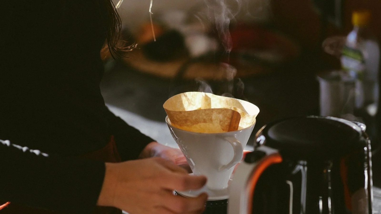 A person making pour-over coffee in a kitchen in the morning