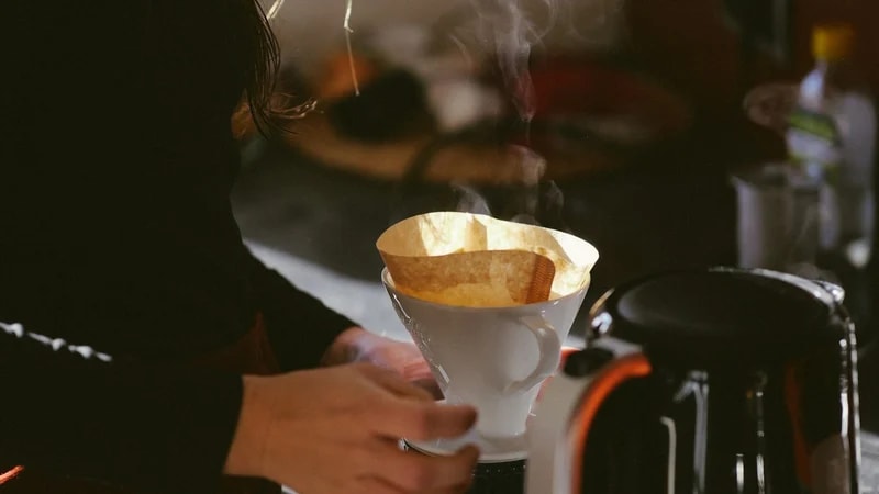 A person making pour-over coffee in a kitchen in the morning