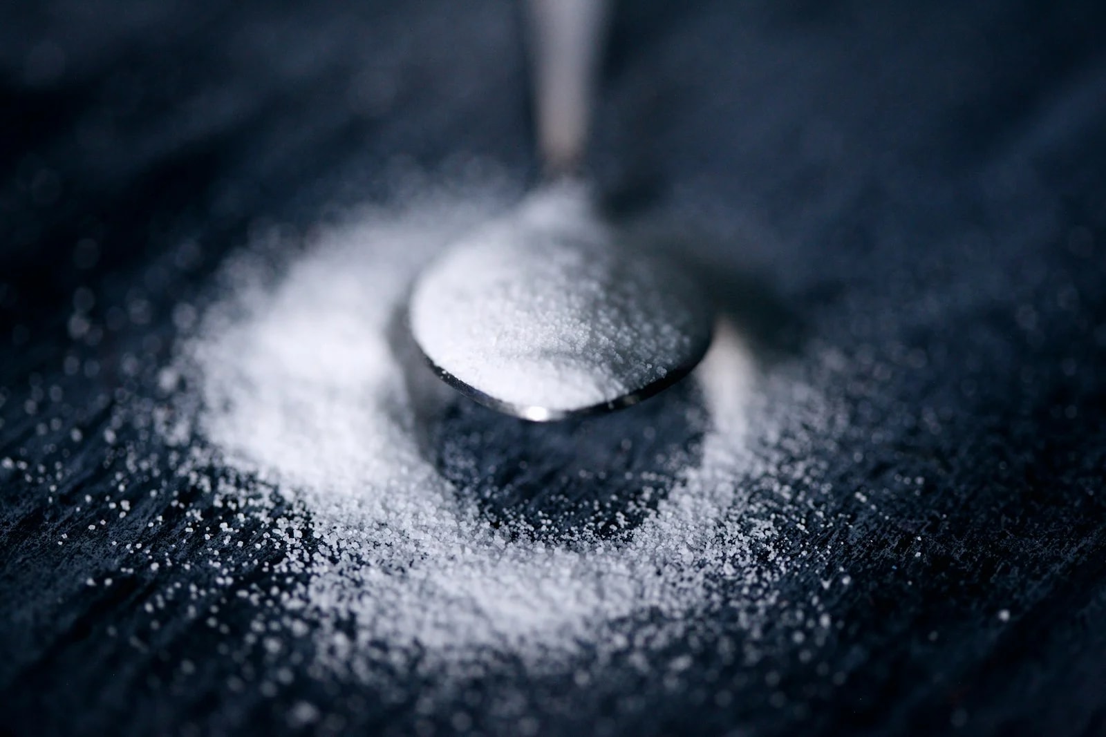 A spoonful of fine white powder spilling onto a dark table