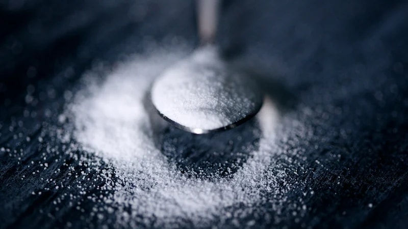 A spoonful of fine white powder spilling onto a dark table