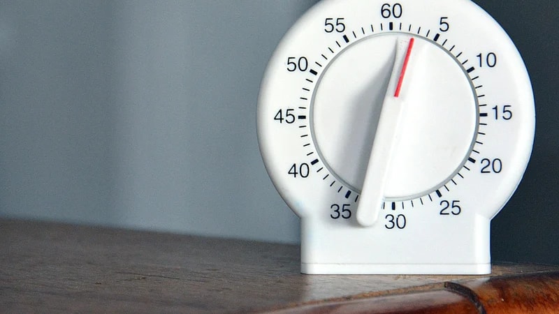 A white analog kitchen timer with a dial from 0 to 60 minutes on a wooden table