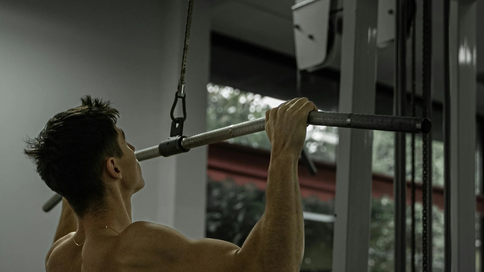 Homem sem camisa fazendo puxada frontal na polia alta de uma academia