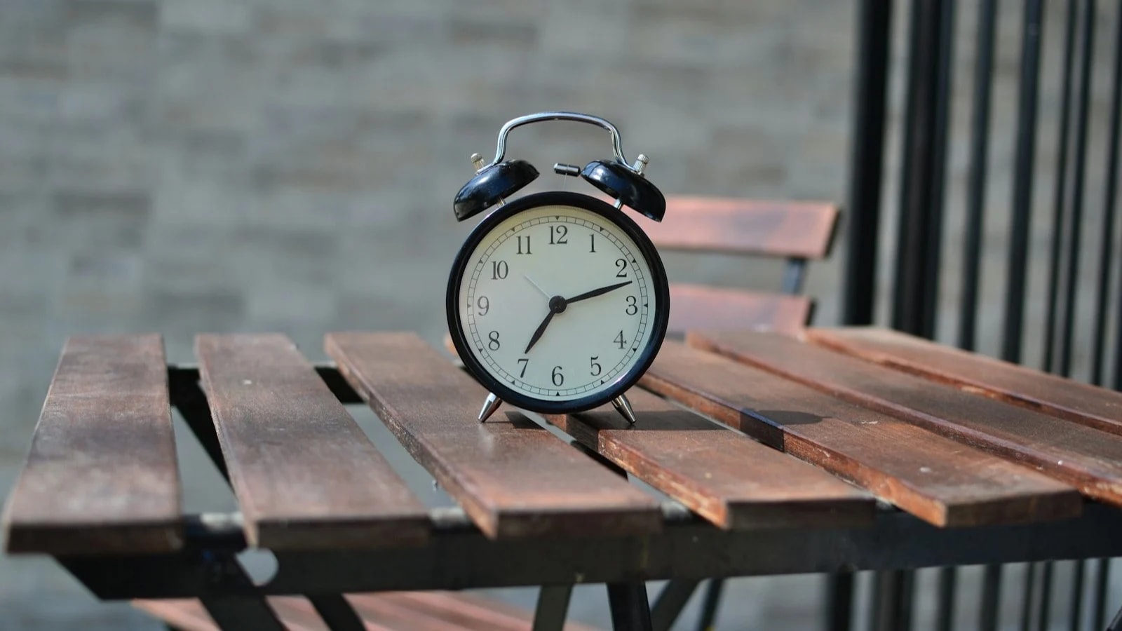 A black twin-bell alarm clock in morning sunlight on a wooden outdoor table