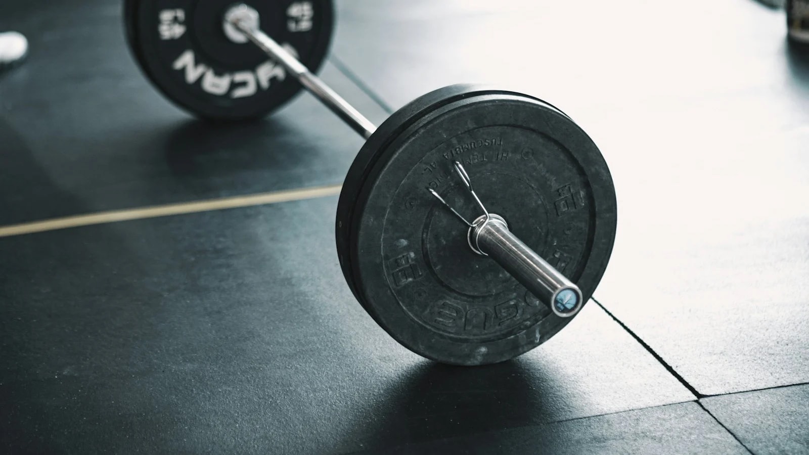 A barbell with a single plate resting on a gym floor
