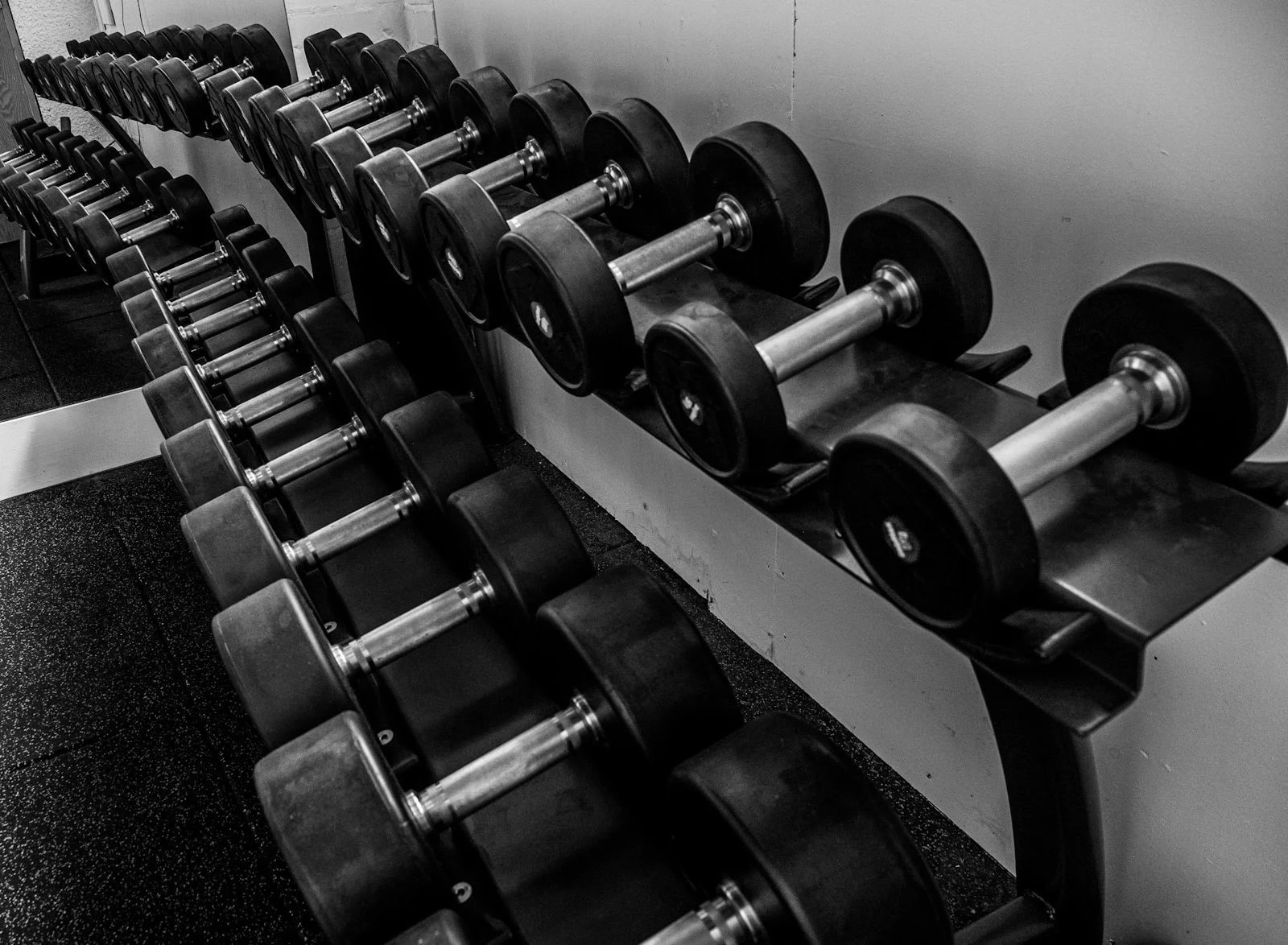 A black and white photo of dumbbells arranged by weight on a rack