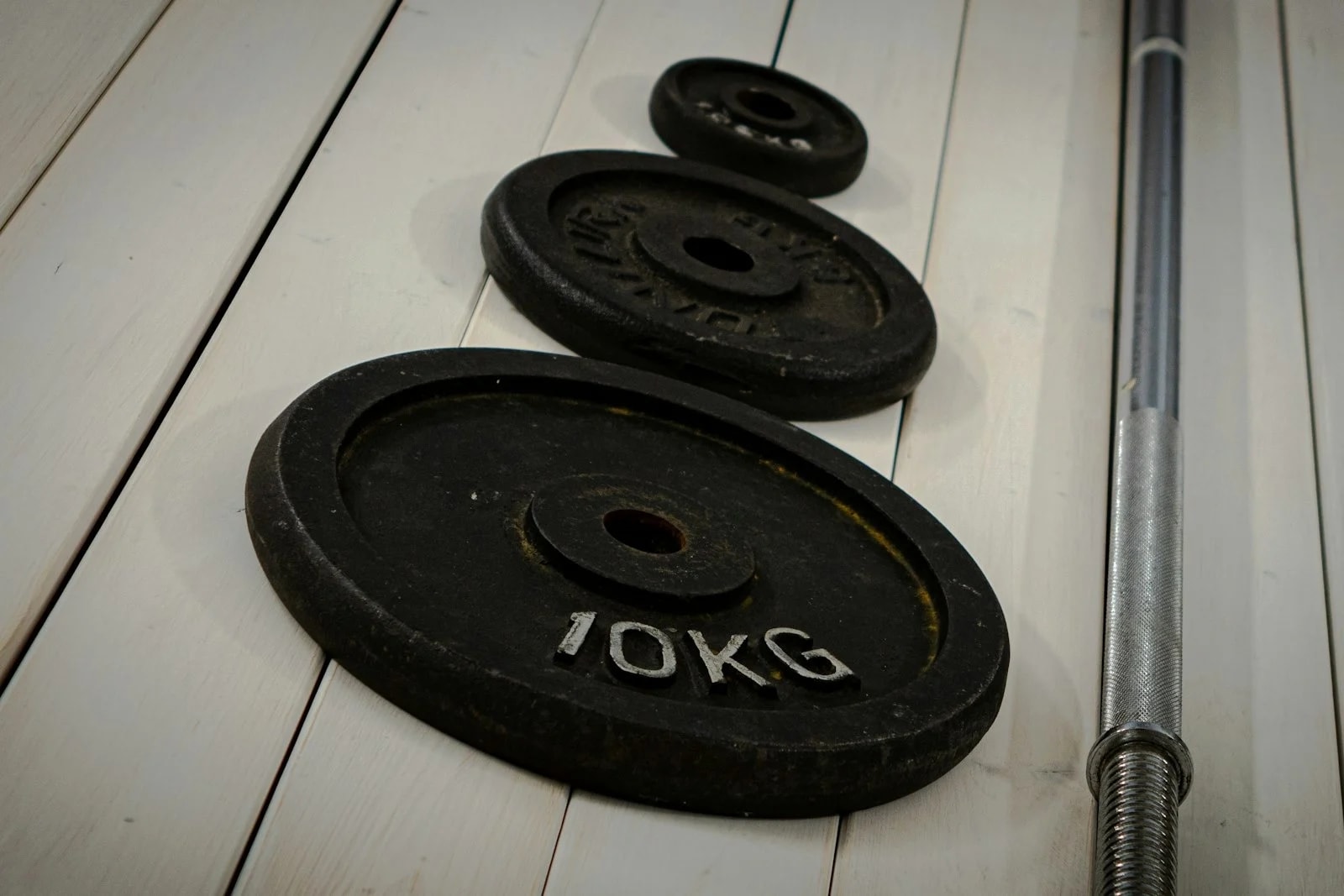 Two iron weight plates and a barbell on a wooden floor