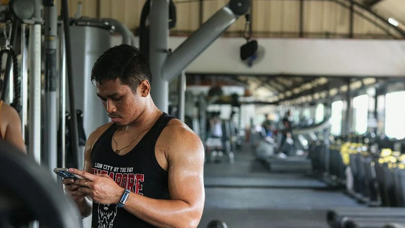 A man in a tank top checking his phone between sets in a gym