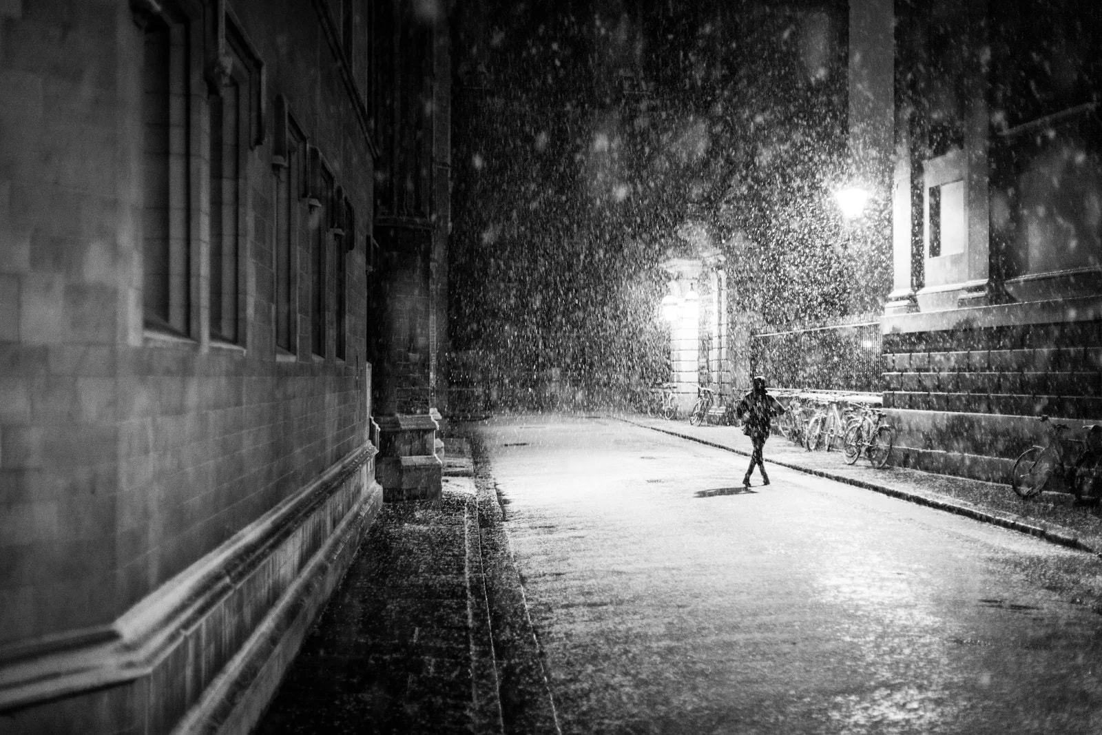 A person running down a narrow city street at night in heavy rain, in black and white