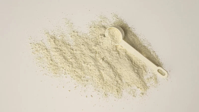 A small white scoop resting in a wide spread of pale powder on a white surface