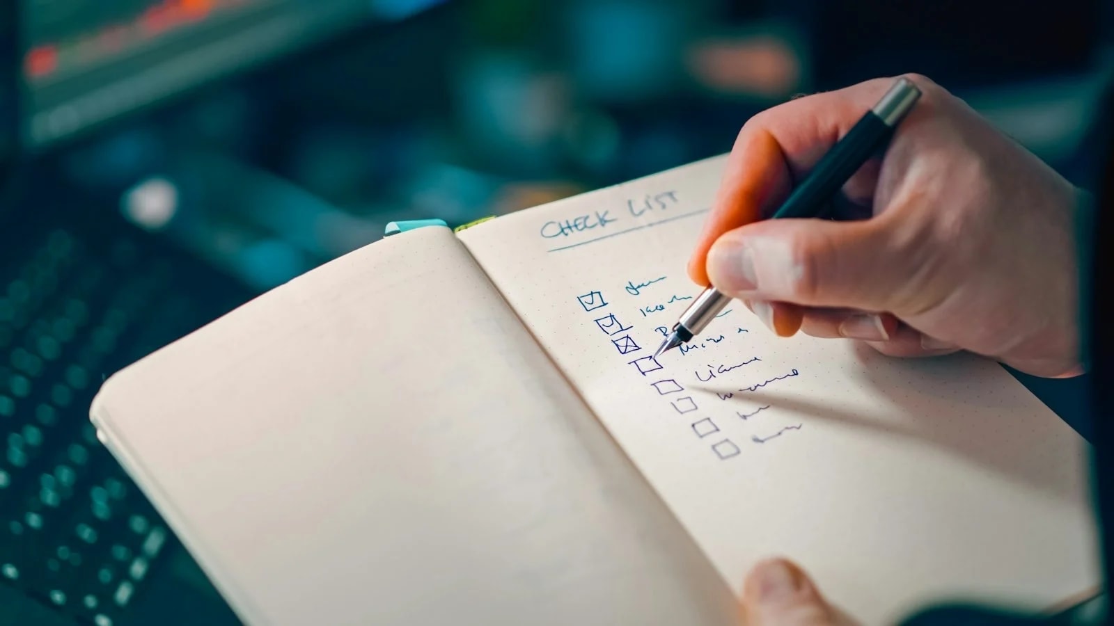A hand ticking boxes on a handwritten checklist in a notebook