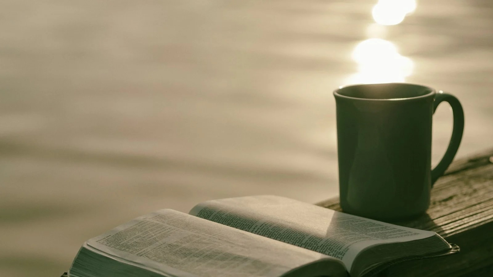 A green mug next to an open book on a table in soft morning light