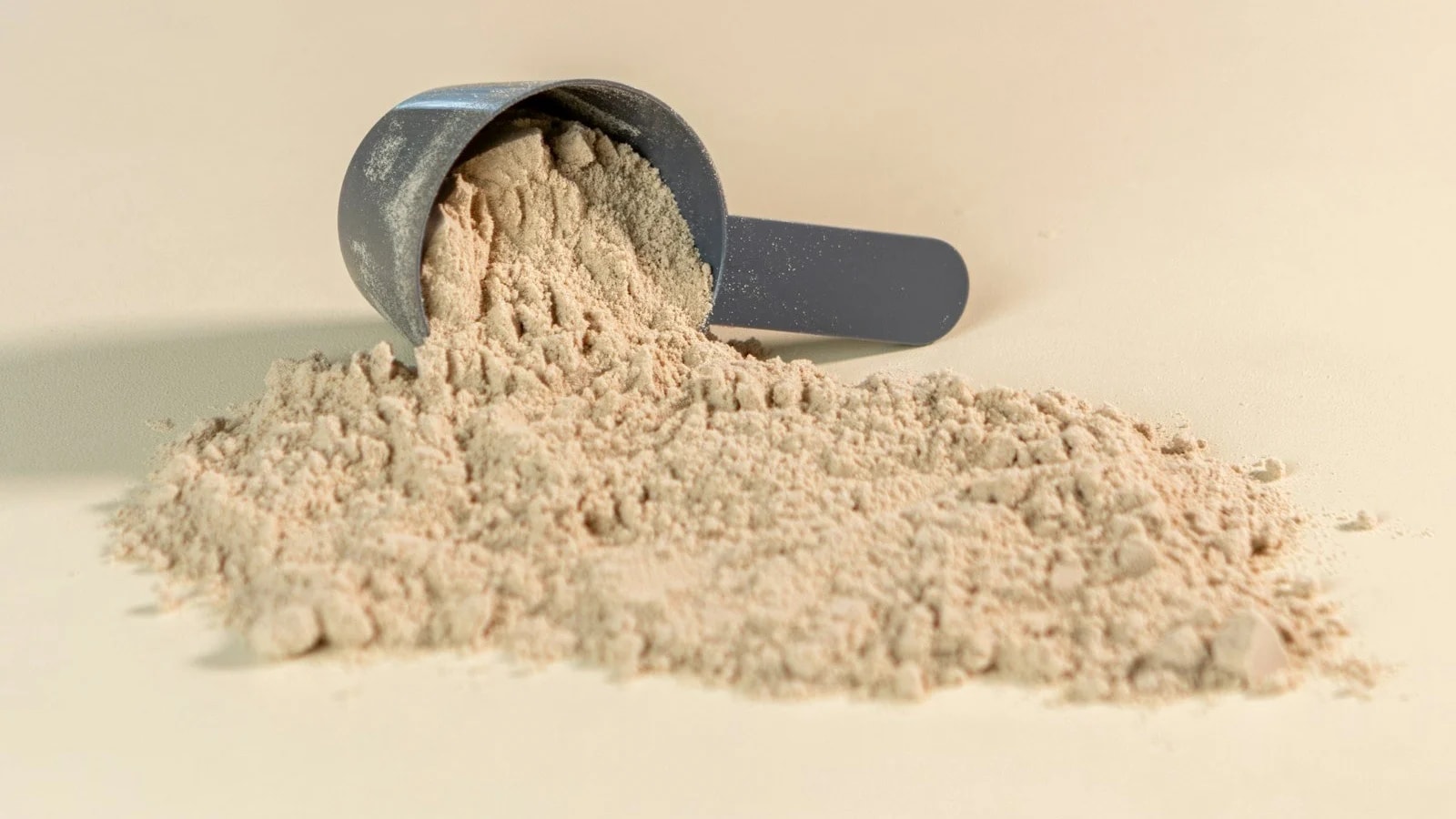 A dark scoop tipped over with powder spilling onto a cream surface